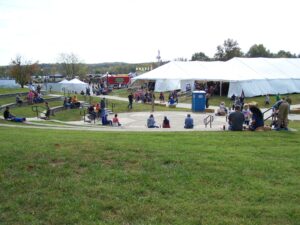 Families enjoy Heritage Days at Drake Harbor in Warsaw, MO, with a large white event tent and outdoor seating.
